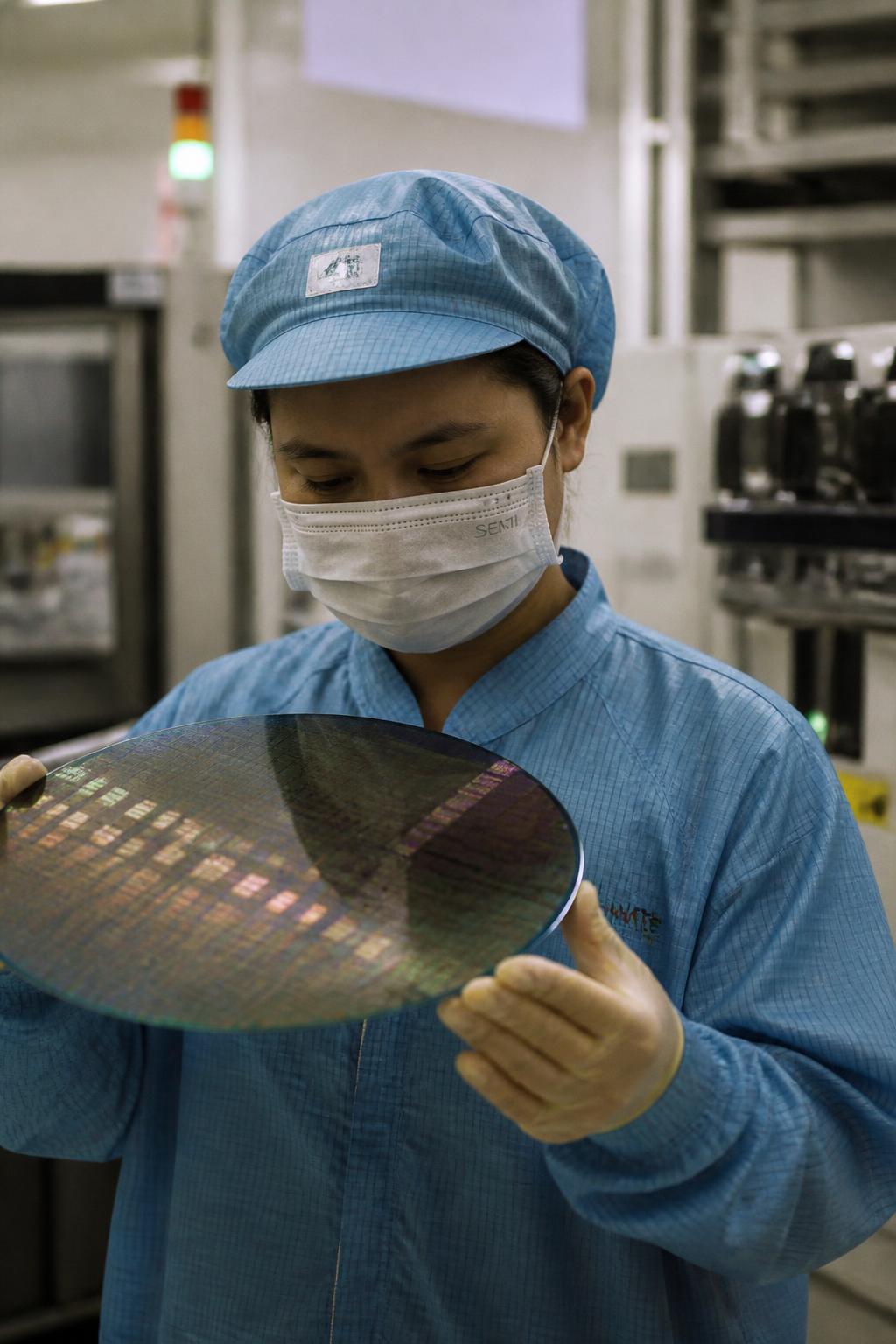 Kỹ thuật viên kiểm tra tấm wafer silicon trong nhà máy bán dẫn